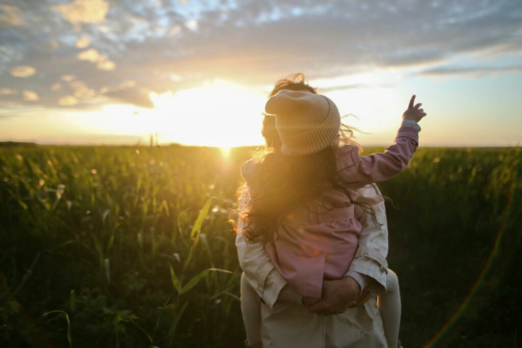 A woman in a field holding her young child in the sunlight.