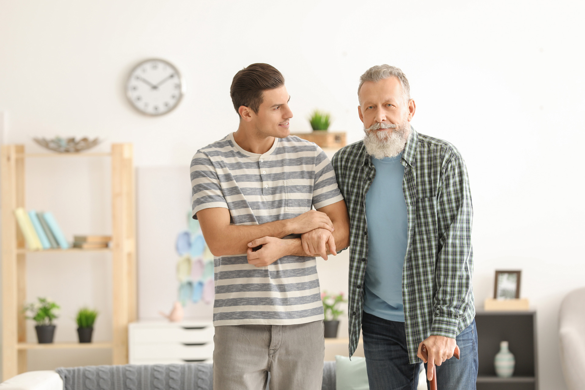 smiling man standing next to and supporting another smiling man with cane