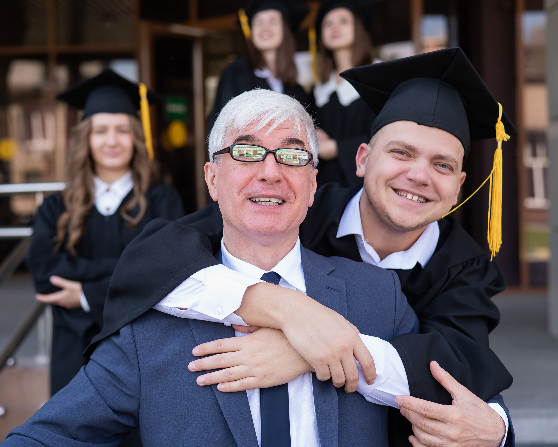 young smiling graduate hugging smiling grandparent from behind