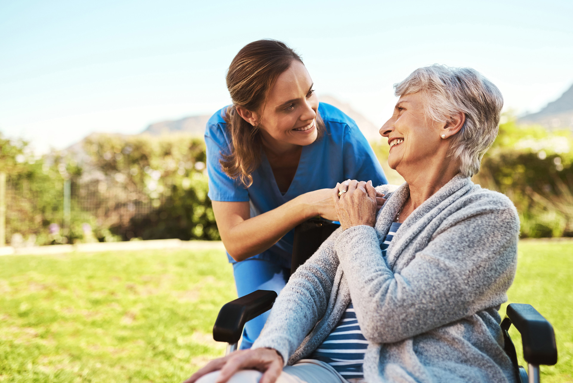 smiling woman in wheelchair with smiling nurse helping her outside