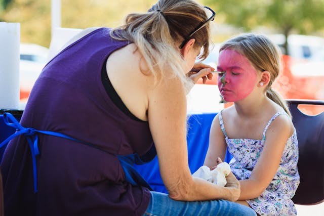 Woman face painting young girl at outdoor event